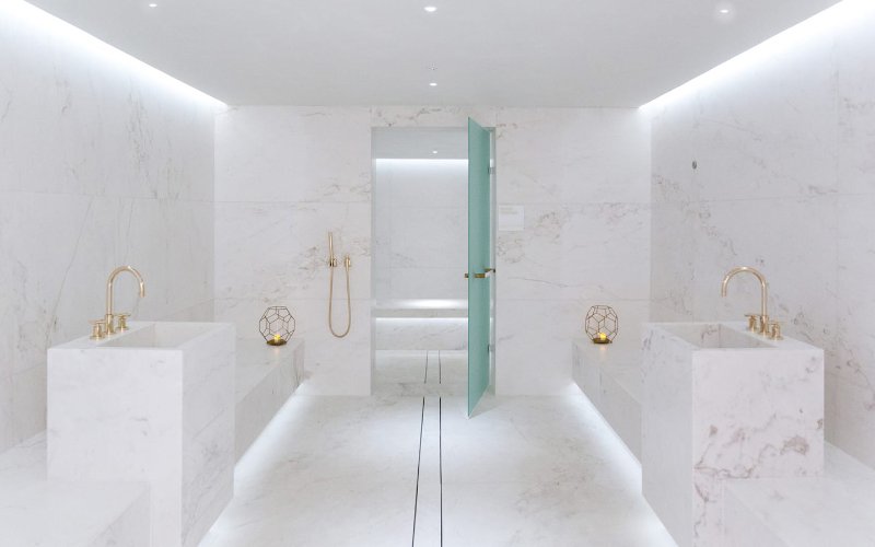 Spa at Four Seasons Hotel at The Surf Club, featuring elegant marble decor with two sinks, a seating area, and a shower surrounded by white marble.