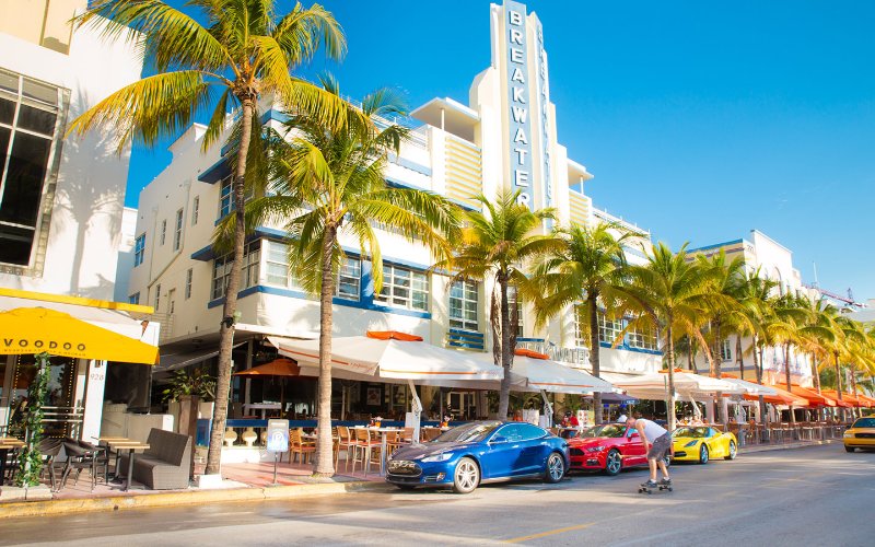 Vibrant and colorful Art Deco hotels along Ocean Drive, in front of the buildings lined up luxury cars in blue, red and yellow
