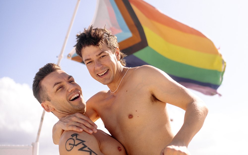 Matt and Michael standing in front of a flag at the beach